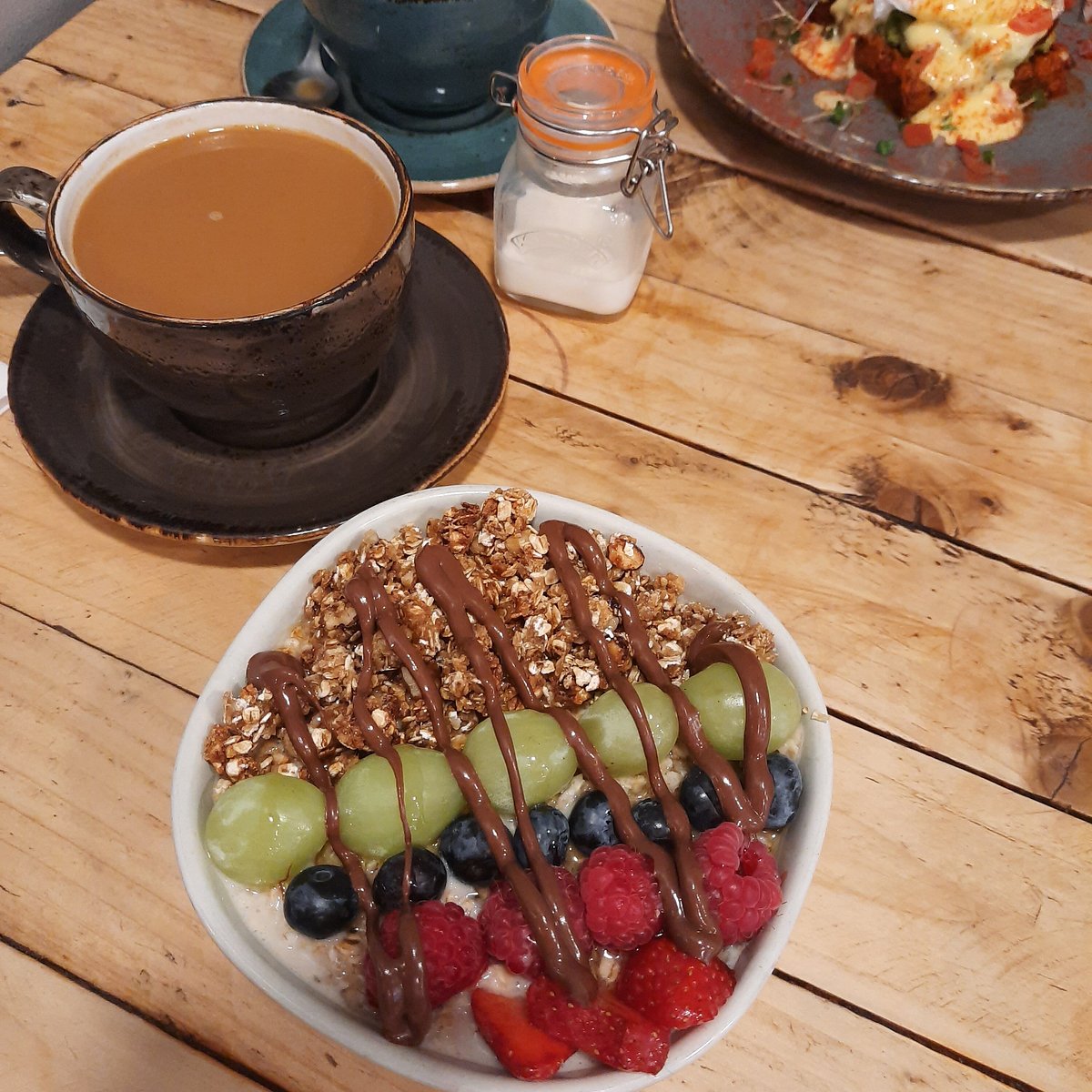 Coffee, granola bowl and another plate arranged on a timber table