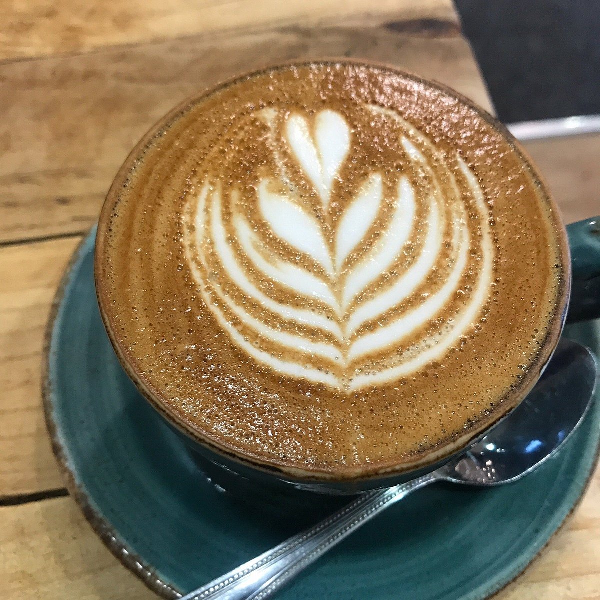 Latte with leaf shaped latte art in a blue green ceramic cup