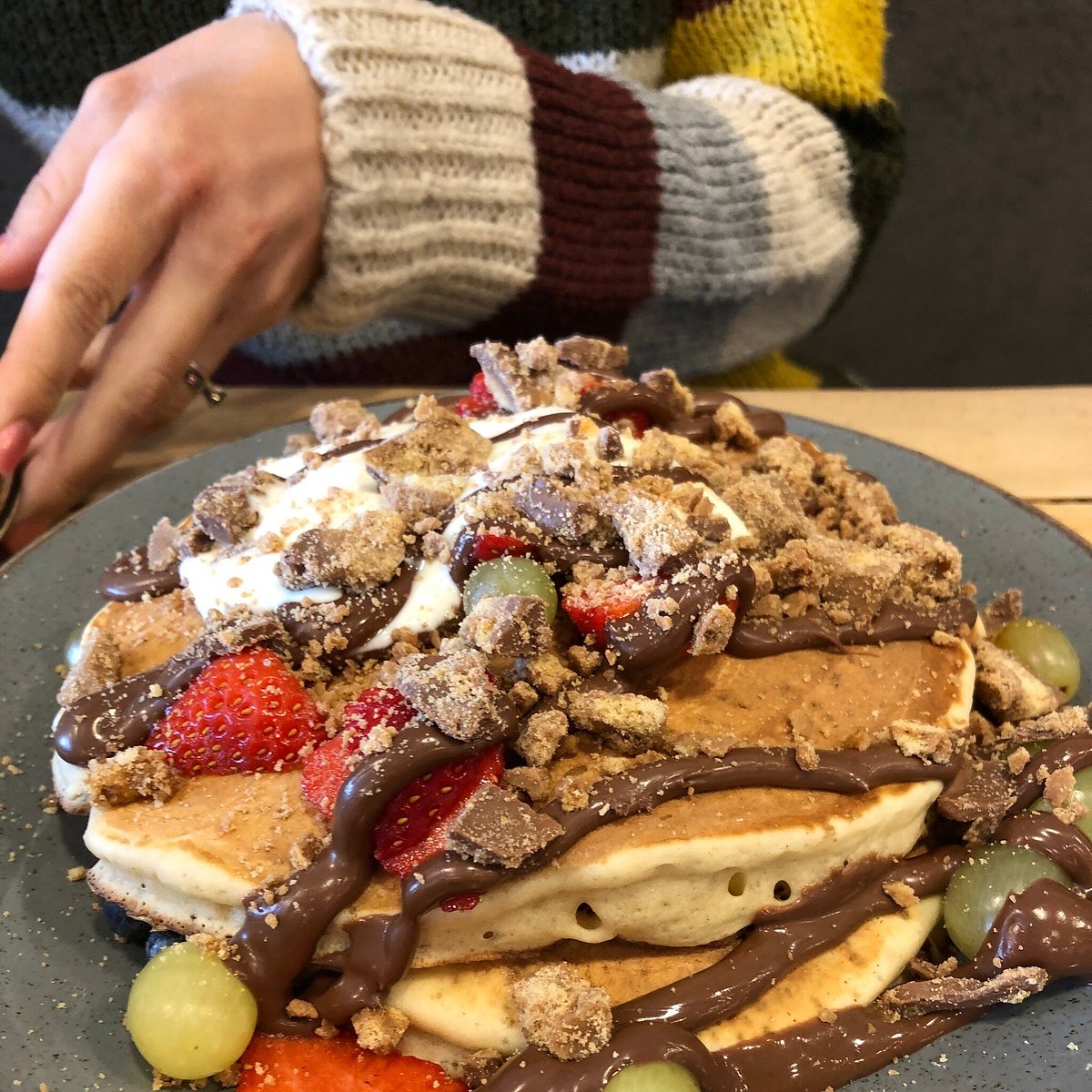 Stack of pancakes topped with fruit, cream and chocolate drizzle
